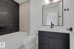 Modern bathroom featuring a deep soaking tub with glossy black subway tile surround, a sleek black vanity with integrated sink, a large framed mirror, and brushed metal fixtures - 