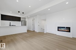 Open-concept living area featuring light wood-finish flooring, recessed ceiling lighting, a contemporary linear fireplace, and a kitchen island with a black matte faucet - 