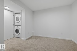 Dedicated laundry closet featuring a stacked washer and dryer unit, set within a neutral-toned room with carpet flooring and crisp white walls - 