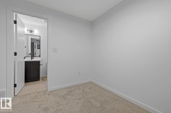 Neutral-toned carpeted room with light gray walls, a white baseboard, and a doorway leading to a bathroom - 