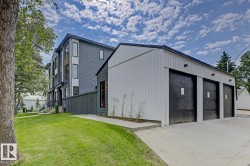 Contemporary multi-level residence featuring dark gray siding, large vertical windows, and a three-bay detached garage with white paneling and black doors - 
