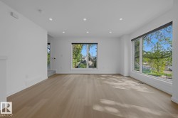 Bright living area featuring wide-plank wood-finish flooring, recessed ceiling lighting, and large windows with black trim - 
