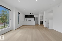 Bright open-concept living space with expansive windows, light wood-finish flooring, recessed lighting, and a modern kitchen featuring an island, dark cabinetry, and stainless steel appliances - 