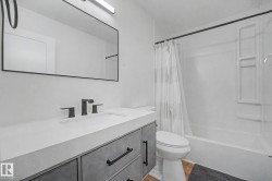 Contemporary bathroom featuring a vanity with a white countertop and integrated sink, matte black faucet, and a large black-framed mirror - 