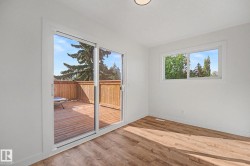 Spacious room featuring wood-finish flooring, a large window, and a sliding glass door providing direct access to an outdoor deck - 