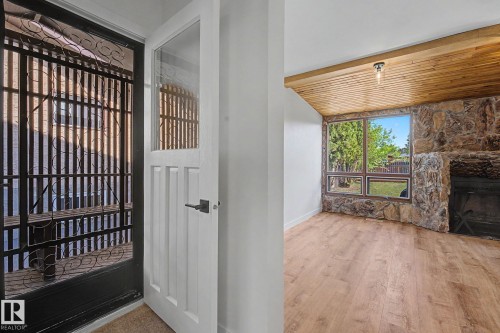 Entryway featuring a white paneled door with glass insert, black security door, and wood-finish flooring - 60 Mcnabb Crescent, Stony Plain, AB - Indoor Photo Showing Other Room With Fireplace
