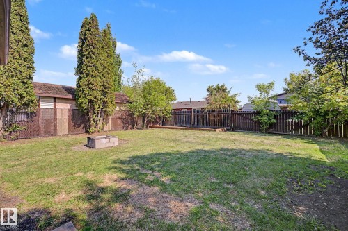 Spacious grassy yard featuring mature trees, a wood privacy fence, and an integrated fire pit constructed from concrete blocks - 60 Mcnabb Crescent, Stony Plain, AB - Outdoor