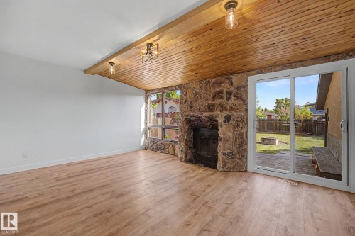 Living area featuring wood-finish flooring, a stone accent wall with a built-in fireplace, a wood-paneled ceiling with exposed beams and recessed lighting, and a sliding glass door providing outdoor access - 60 Mcnabb Crescent, Stony Plain, AB - Indoor With Fireplace