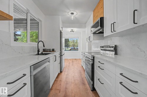 Galley kitchen featuring white shaker cabinetry, stainless steel appliances, wood-finish flooring, white countertops with integrated sink, and matte black fixtures - 60 Mcnabb Crescent, Stony Plain, AB - Indoor Photo Showing Kitchen With Upgraded Kitchen