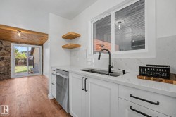 Modern kitchen featuring white shaker cabinetry with matte black hardware, stone-finish countertops, and a stainless steel dishwasher - 