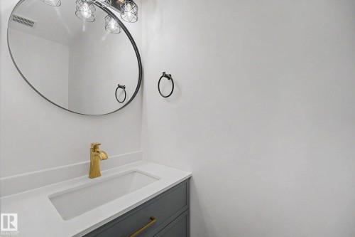 Bathroom vanity featuring a gold-finish faucet, integrated rectangular sink, white countertop, and gray cabinetry with gold-finish hardware - 60 Mcnabb Crescent, Stony Plain, AB - Indoor Photo Showing Bathroom