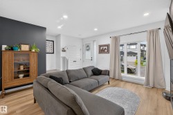 Open concept living area featuring light wood-finish flooring, recessed ceiling lighting, and a prominent large window with white trim - 
