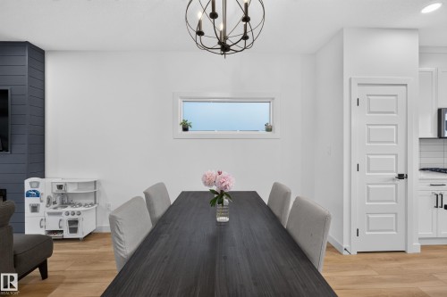 Spacious dining area featuring a contemporary dark wood-finish table, a decorative chandelier, light wood-finish flooring, and a horizontal window - 548 Kleins Crescent, Leduc, AB 
