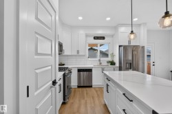 Bright kitchen featuring white cabinetry, stainless steel appliances, a center island with a light-toned countertop, wood-finish flooring, and pendant lighting - 