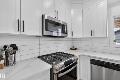 Modern kitchen featuring white shaker-style cabinetry, stainless steel appliances, white subway tile backsplash, and light-toned countertops - 548 Kleins Crescent, Leduc, AB 