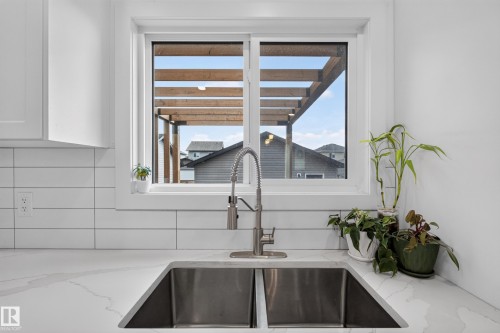 Kitchen sink featuring a dual-basin stainless steel sink with a pull-down faucet, set into a white countertop with subtle veining - 548 Kleins Crescent, Leduc, AB 