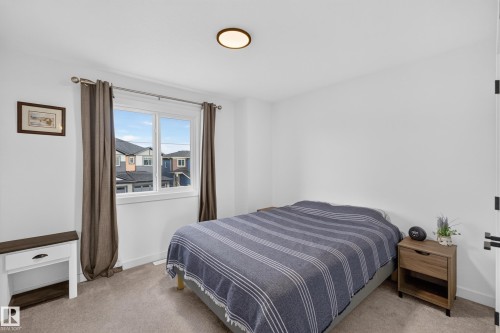 Bright bedroom featuring a large window, plush carpet flooring, white baseboards, and a flush mount ceiling light - 548 Kleins Crescent, Leduc, AB 