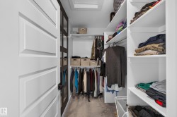 Custom closet organization system featuring white shelving, multiple hanging rods, and recessed lighting - 