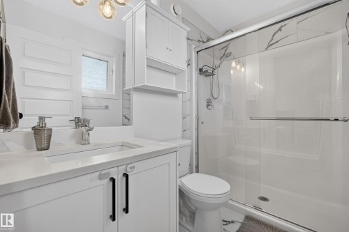 Contemporary bathroom featuring a glass-enclosed shower, white vanity with black hardware, integrated sink, and white marble-look wall tiles - 548 Kleins Crescent, Leduc, AB 