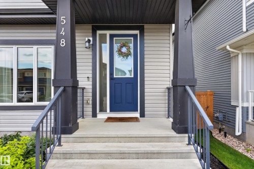 Modern facade featuring light gray siding with contrasting dark trim and a vibrant blue entry door - 548 Kleins Crescent, Leduc, AB 