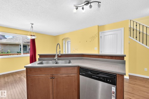 Kitchen island featuring a double basin stainless steel sink with a high-arc faucet, integrated dishwasher, and wood-finish cabinetry - 211 59 Street, Edmonton, AB 