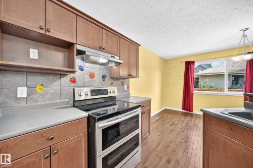 Kitchen featuring wood-finish flooring, ample cabinetry, a built-in range with an overhead microwave, a window, and a sink - 211 59 Street, Edmonton, AB 