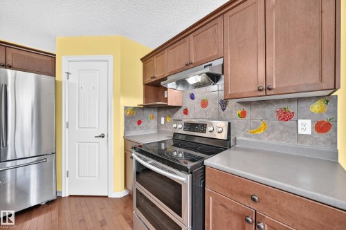 Kitchen featuring a stainless steel electric range, stainless steel refrigerator, and wood-finish cabinetry - 211 59 Street, Edmonton, AB 