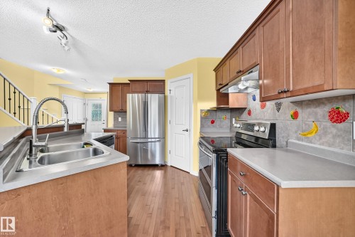 Kitchen featuring wood-finish flooring, light wood cabinetry, stainless steel appliances, a dual basin sink with a high-arc faucet, and tiled backsplash - 211 59 Street, Edmonton, AB 