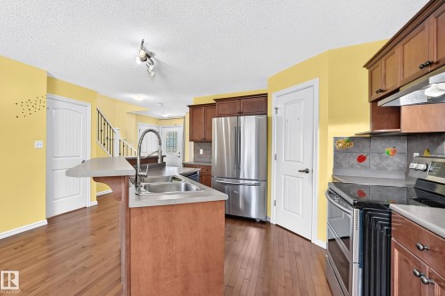 Kitchen featuring wood-finish flooring, stainless steel appliances, dark wood cabinetry, a double basin sink, and a tile backsplash - 211 59 Street, Edmonton, AB 