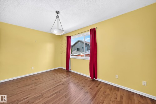 Spacious room featuring wood-finish flooring, light yellow walls, and a large window - 211 59 Street, Edmonton, AB 