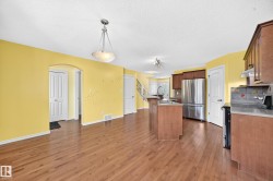 Open-concept kitchen and living area featuring wood-finish flooring, a central island with an integrated sink, stainless steel refrigerator, wood cabinetry, and an arched entryway - 