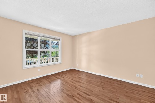 Spacious room featuring wood-finish flooring, light beige walls, white baseboards, and a large multi-pane window with white trim - 211 59 Street, Edmonton, AB 