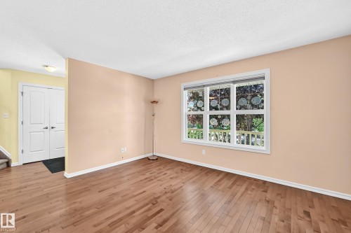 Open concept living area featuring wood-finish flooring, a large multi-pane window, and neutral wall tones - 211 59 Street, Edmonton, AB 
