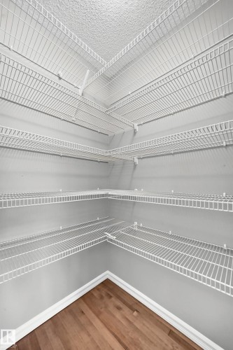 Corner pantry featuring multiple white wire shelving units and wood-finish flooring - 211 59 Street, Edmonton, AB 