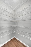 Corner pantry featuring multiple white wire shelving units and wood-finish flooring - 