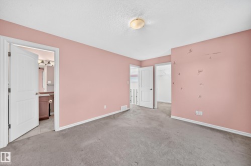 Carpeted room with a flush-mount ceiling light fixture, featuring a doorway to a bathroom with tile flooring and a vanity, and a separate doorway leading to a walk-in closet - 211 59 Street, Edmonton, AB 