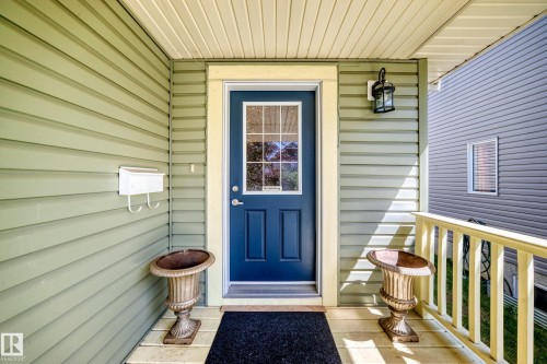 Entryway featuring a deep blue door with decorative glass inserts, pale green horizontal siding, and a contrasting cream-colored ceiling and trim - 211 59 Street, Edmonton, AB 