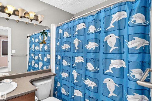 Bathroom featuring a shower curtain rod, a vanity mirror, a wall-mounted light fixture with five sconces, a built-in grab bar, and a single-handle faucet - 211 59 Street, Edmonton, AB 