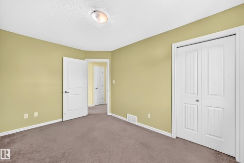 Carpeted room featuring a white interior door, bifold closet doors with vertical paneling, light green walls, and white baseboards - 211 59 Street, Edmonton, AB 