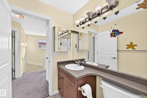 Full bathroom featuring a single vanity with an integrated sink and brown cabinetry, framed by a multi-bulb vanity light fixture - 211 59 Street, Edmonton, AB 
