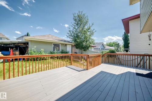 Expansive multi-level wood-finish deck with natural wood railings, overlooking a grassy yard with mature foliage - 211 59 Street, Edmonton, AB 