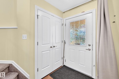 Entryway featuring a white paneled door with textured glass insert, adjacent double closet doors, and wood-finish flooring - 211 59 Street, Edmonton, AB 