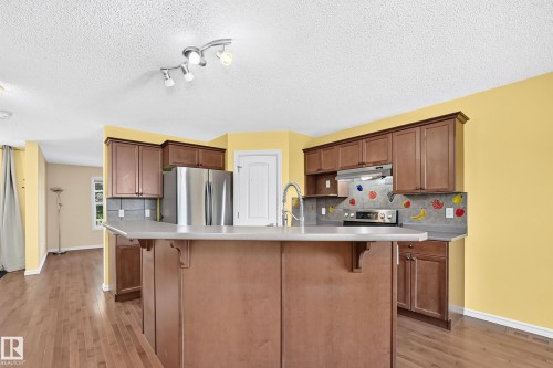 Kitchen featuring wood-finish cabinetry, stainless steel appliances, an island with an integrated sink, and track lighting - 211 59 Street, Edmonton, AB 