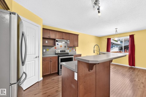 Kitchen featuring wood-finish flooring, warm yellow walls, and a peninsula with an integrated sink and gooseneck faucet - 211 59 Street, Edmonton, AB 
