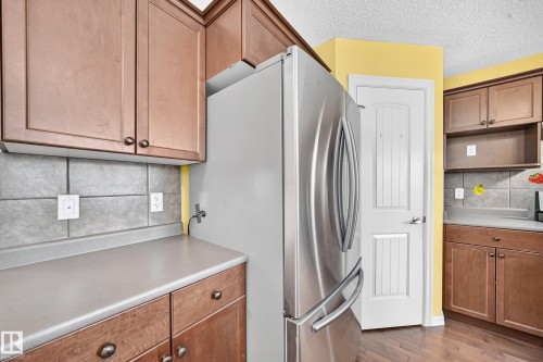 Contemporary kitchen featuring medium-tone wood cabinetry, gray countertops, and a tiled backsplash - 211 59 Street, Edmonton, AB 