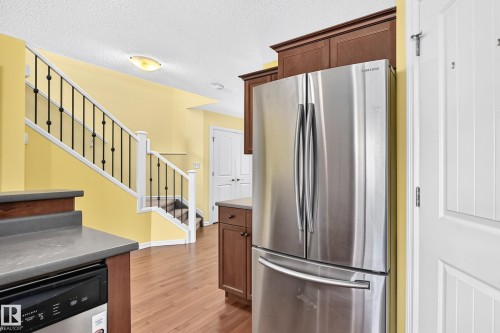 Kitchen area featuring a stainless steel French door refrigerator, dark wood-finish cabinetry, and a gray countertop - 211 59 Street, Edmonton, AB 
