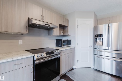 Kitchen featuring wood-finish cabinetry, stainless steel appliances, light-toned countertops, and a subway tile backsplash - 16627 18 Avenue, Edmonton, AB 