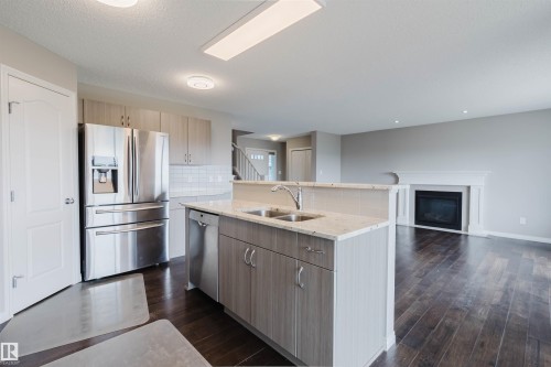 Modern kitchen with a central island featuring a double-basin stainless steel sink and integrated dishwasher - 16627 18 Avenue, Edmonton, AB 