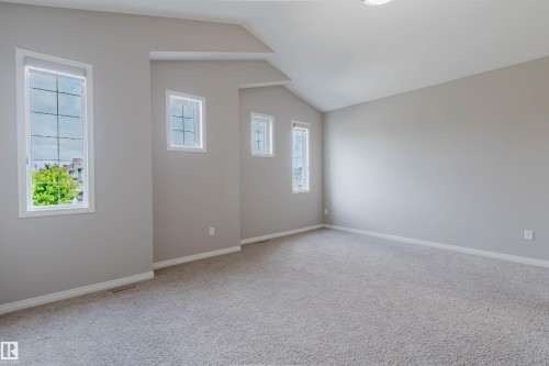 Spacious room featuring vaulted ceilings, light gray wall tones, plush gray carpeting, and multiple windows with white trim - 16627 18 Avenue, Edmonton, AB 