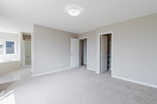 Carpeted room with a ceiling-mounted light fixture, leading to a bathroom featuring a built-in bathtub, a shower enclosure, and a window with horizontal blinds - 16627 18 Avenue, Edmonton, AB 